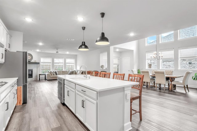 kitchen featuring a kitchen bar, sink, hanging light fixtures, a center island with sink, and white cabinets