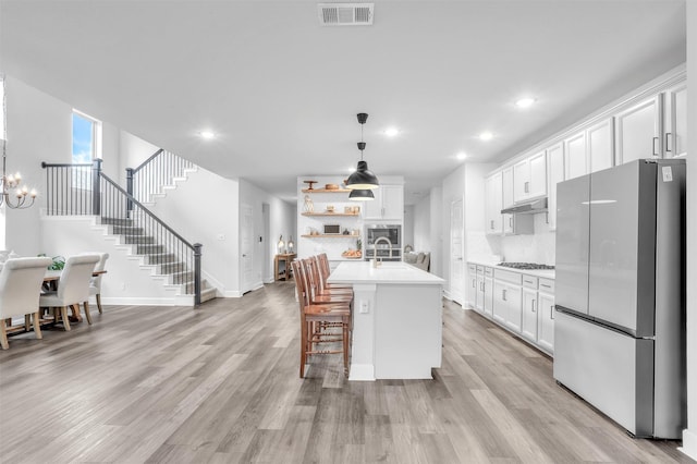 kitchen featuring a breakfast bar, appliances with stainless steel finishes, white cabinetry, an island with sink, and decorative light fixtures