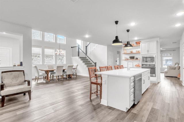 kitchen with appliances with stainless steel finishes, an island with sink, sink, white cabinets, and hanging light fixtures