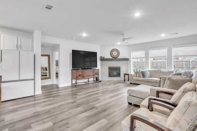 living room with ceiling fan, a tile fireplace, and light hardwood / wood-style flooring