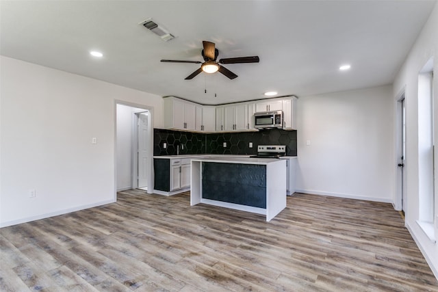 kitchen with appliances with stainless steel finishes, white cabinetry, tasteful backsplash, a kitchen island, and light wood-type flooring