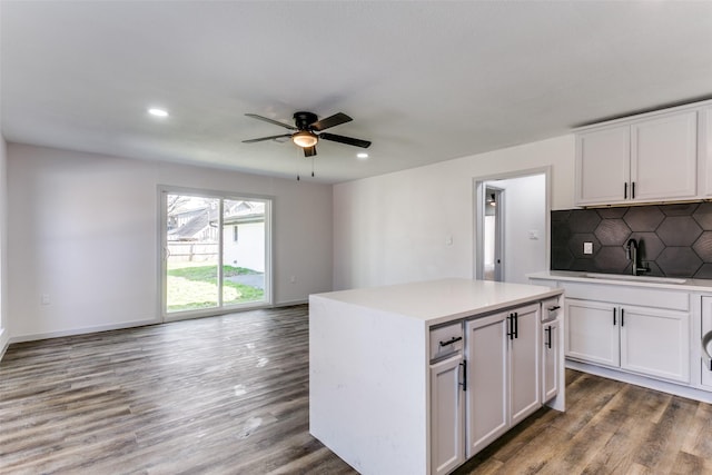 kitchen with tasteful backsplash, white cabinetry, wood-type flooring, sink, and a center island