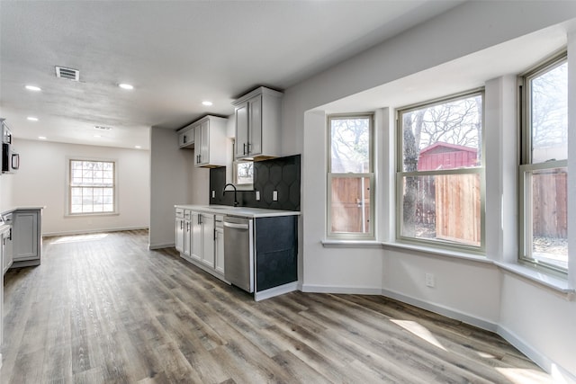 kitchen with dishwasher, sink, gray cabinetry, backsplash, and light hardwood / wood-style flooring