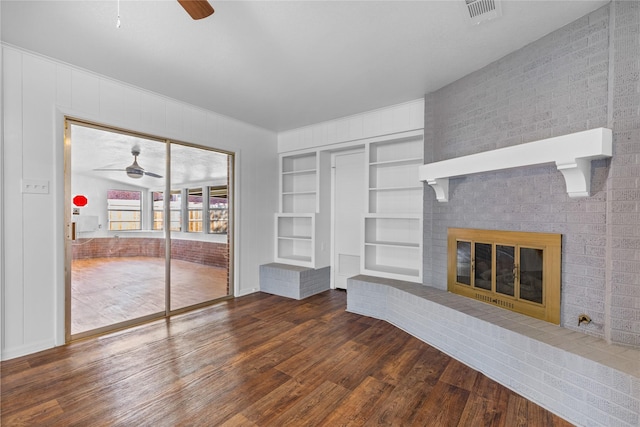 unfurnished living room featuring built in shelves, a fireplace, dark hardwood / wood-style floors, and ceiling fan