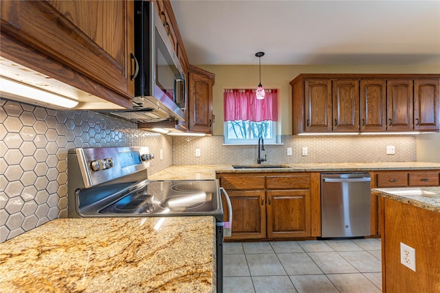 kitchen with light tile patterned flooring, sink, hanging light fixtures, light stone counters, and stainless steel appliances