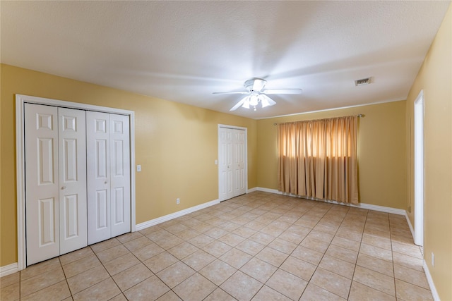 unfurnished bedroom featuring ceiling fan, light tile patterned floors, a textured ceiling, and two closets