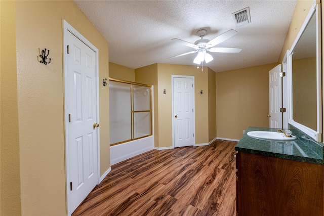 bathroom with hardwood / wood-style floors, shower / bath combination with glass door, vanity, ceiling fan, and a textured ceiling