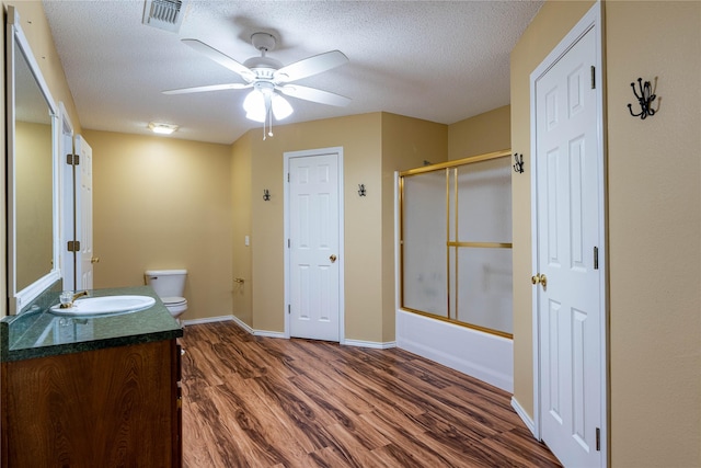 full bathroom featuring hardwood / wood-style flooring, vanity, enclosed tub / shower combo, toilet, and a textured ceiling