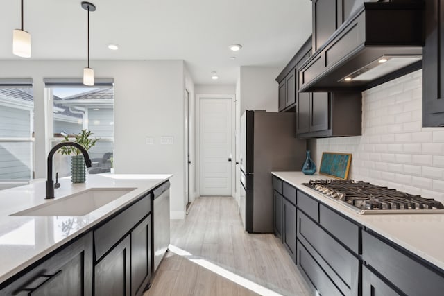 kitchen featuring light wood-style flooring, appliances with stainless steel finishes, custom exhaust hood, light countertops, and a sink