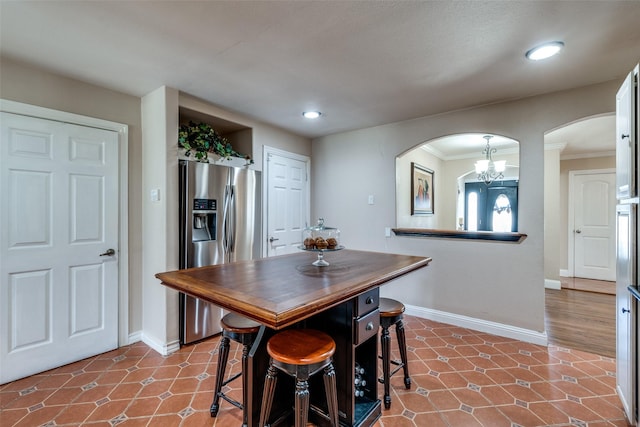 tiled dining space featuring arched walkways, a chandelier, crown molding, and baseboards