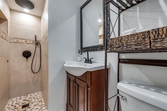 bathroom featuring vanity, toilet, a textured wall, and a tile shower