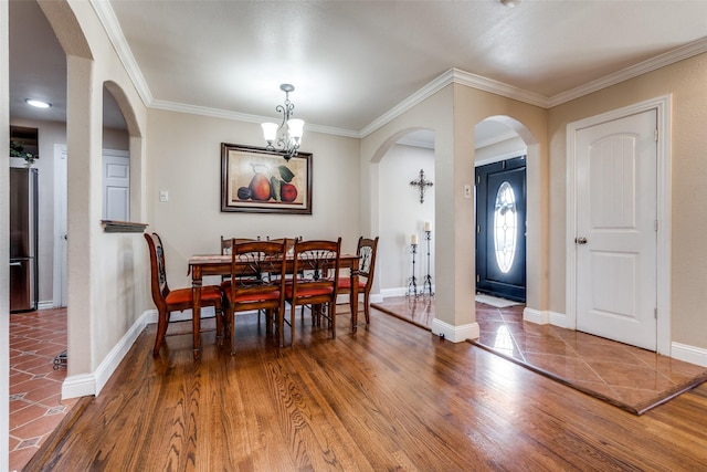 dining space with ornamental molding, wood finished floors, arched walkways, baseboards, and a chandelier