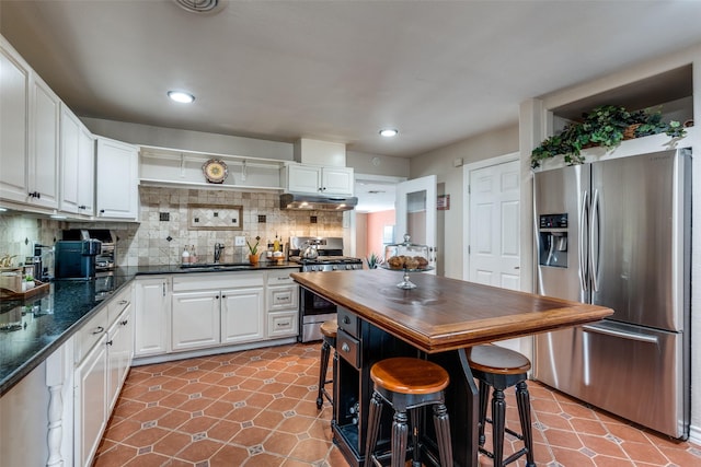 kitchen with under cabinet range hood, wood counters, a sink, backsplash, and appliances with stainless steel finishes