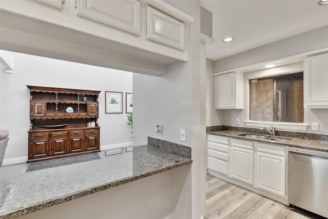 kitchen with white cabinetry, stainless steel dishwasher, sink, and dark stone countertops