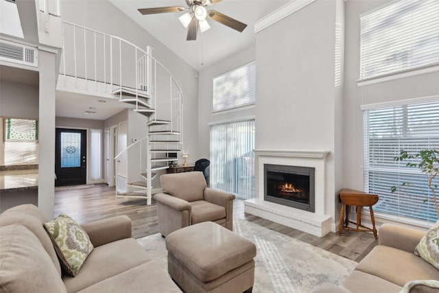 living room featuring a high ceiling, ceiling fan, a brick fireplace, and light wood-type flooring