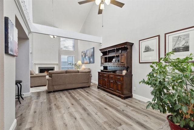 living room with ceiling fan, light hardwood / wood-style floors, and a towering ceiling