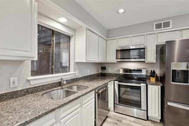 kitchen with appliances with stainless steel finishes, dark stone counters, white cabinets, light hardwood / wood-style floors, and sink