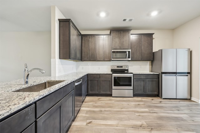 kitchen featuring appliances with stainless steel finishes, sink, backsplash, light hardwood / wood-style floors, and light stone countertops