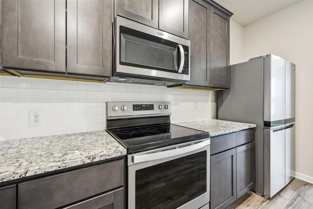 kitchen featuring dark brown cabinetry, sink, stainless steel dishwasher, and light stone countertops