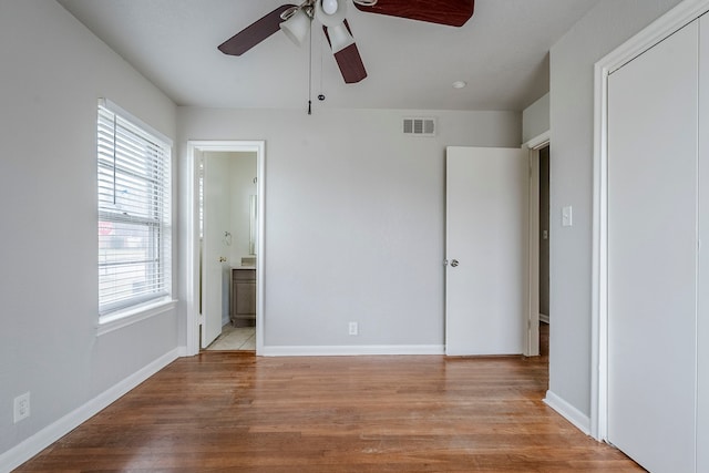 unfurnished bedroom featuring ceiling fan, ensuite bathroom, a closet, and light wood-type flooring