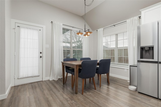 dining space with hardwood / wood-style flooring, vaulted ceiling, and a notable chandelier