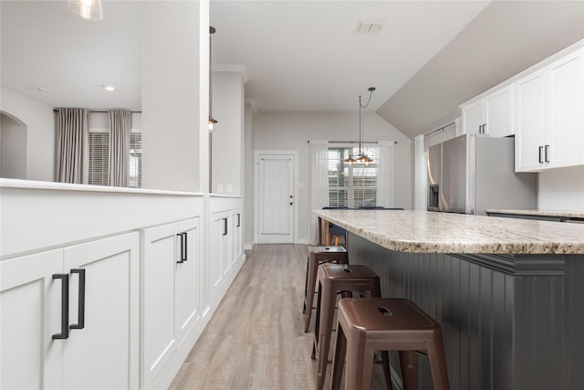 kitchen with light hardwood / wood-style flooring, white cabinets, a kitchen bar, stainless steel fridge with ice dispenser, and decorative light fixtures