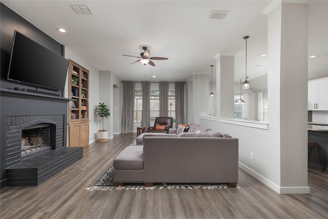 living room with a brick fireplace, dark wood-type flooring, built in features, and ceiling fan