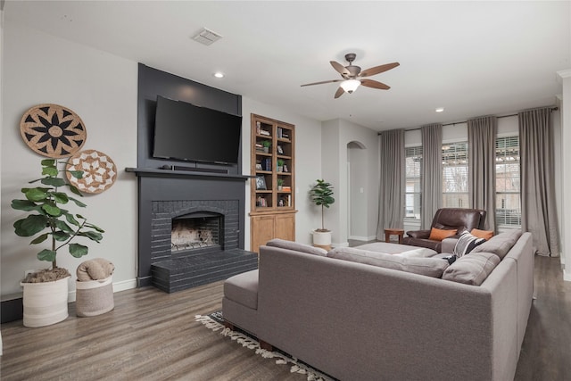 living room with ceiling fan, wood-type flooring, a brick fireplace, and built in features