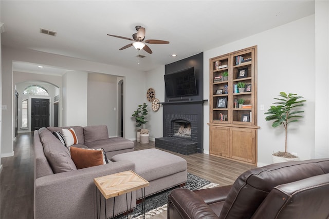 living room featuring wood-type flooring, a brick fireplace, ceiling fan, and built in shelves