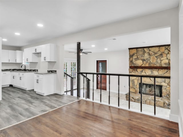 kitchen featuring a stone fireplace, sink, hardwood / wood-style flooring, ceiling fan, and white cabinets