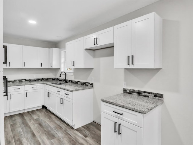 kitchen with white cabinetry, light stone countertops, sink, and light hardwood / wood-style floors