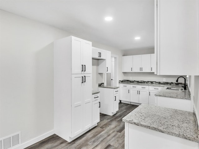 kitchen featuring a kitchen island, hardwood / wood-style floors, white cabinetry, sink, and light stone counters