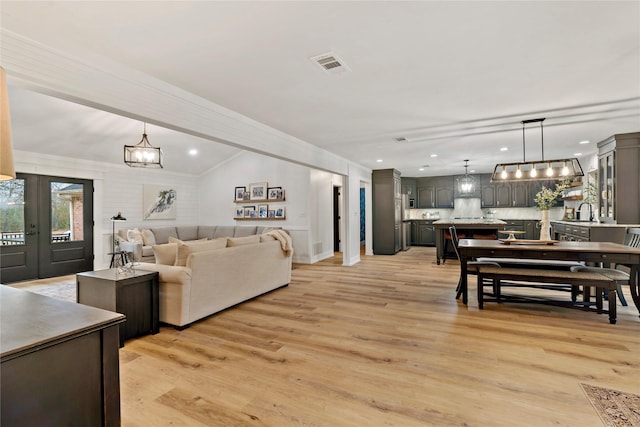 living room with sink, crown molding, french doors, a chandelier, and light wood-type flooring