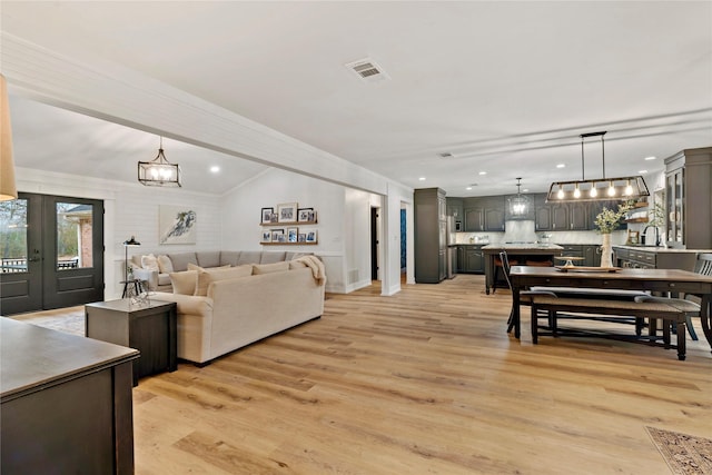living area featuring recessed lighting, light wood finished floors, visible vents, french doors, and a notable chandelier