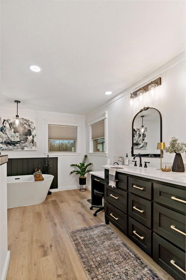 full bathroom with wood finished floors, vanity, a soaking tub, baseboards, and recessed lighting