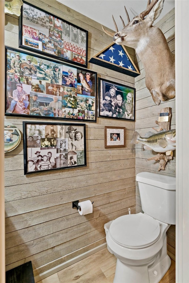 half bath featuring wooden walls, toilet, and wood finished floors