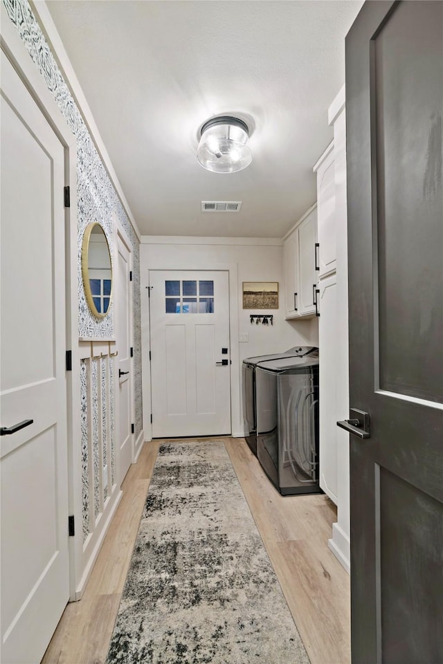 laundry area featuring ornamental molding, cabinets, washing machine and clothes dryer, and light wood-type flooring