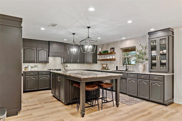 kitchen featuring a kitchen island, a breakfast bar, open shelves, light wood-style flooring, and a sink