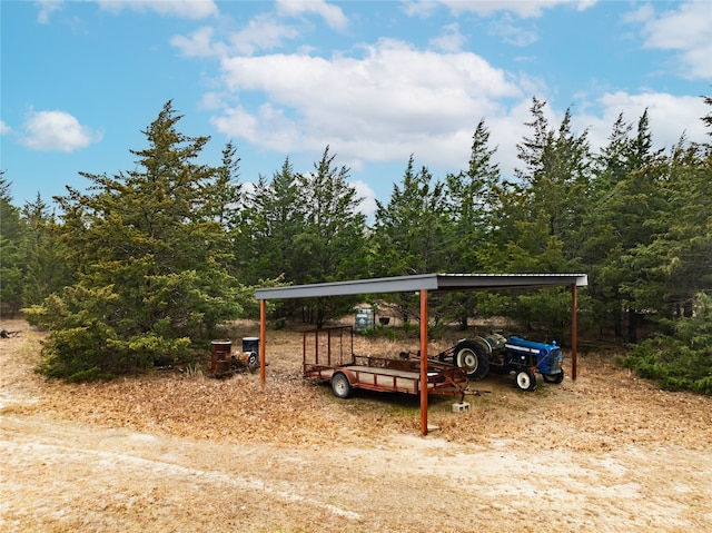 view of yard featuring a carport, a view of trees, and dirt driveway