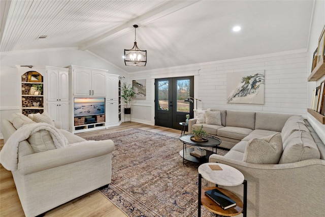living room featuring lofted ceiling with beams, french doors, a chandelier, and light wood-type flooring