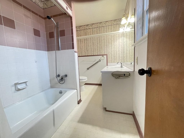 bathroom featuring toilet, tub / shower combination, vanity, baseboards, and wallpapered walls