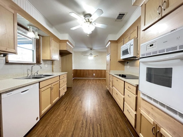 kitchen with light brown cabinets, a wainscoted wall, white appliances, a sink, and wallpapered walls