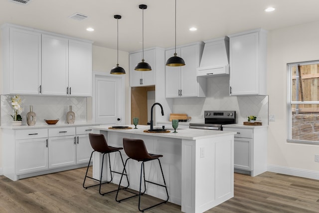 kitchen with hanging light fixtures, stainless steel electric stove, custom range hood, and white cabinetry