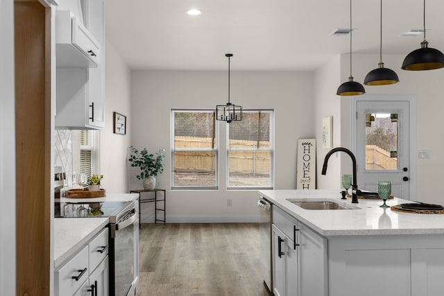 kitchen with sink, appliances with stainless steel finishes, white cabinetry, hanging light fixtures, and light stone countertops