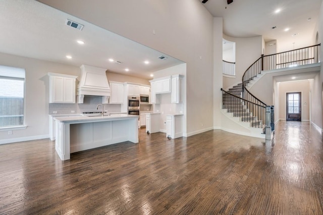 kitchen featuring dark hardwood / wood-style floors, white cabinetry, sink, custom exhaust hood, and a kitchen island with sink