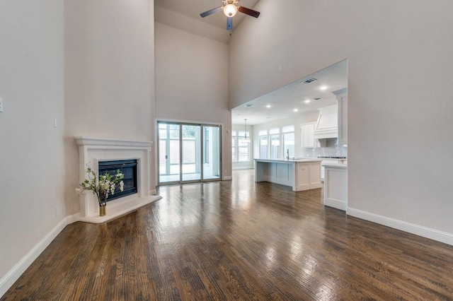 unfurnished living room with sink, high vaulted ceiling, dark hardwood / wood-style floors, ceiling fan, and a fireplace