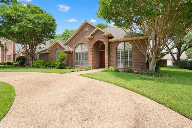 traditional-style house featuring brick siding, a front yard, and a shingled roof