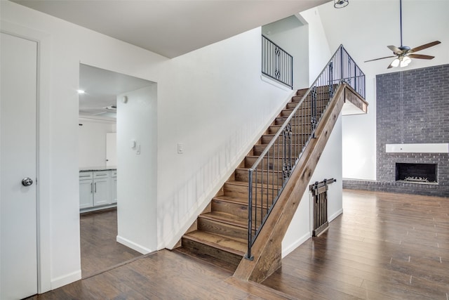 stairway with ceiling fan, a fireplace, hardwood / wood-style floors, and a towering ceiling