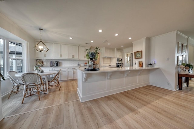 kitchen featuring pendant lighting, tasteful backsplash, white cabinets, kitchen peninsula, and light hardwood / wood-style flooring