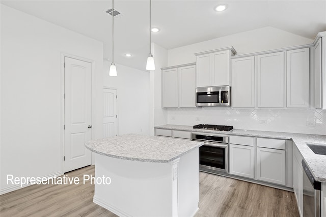 kitchen with pendant lighting, stainless steel appliances, a kitchen island, and light hardwood / wood-style flooring